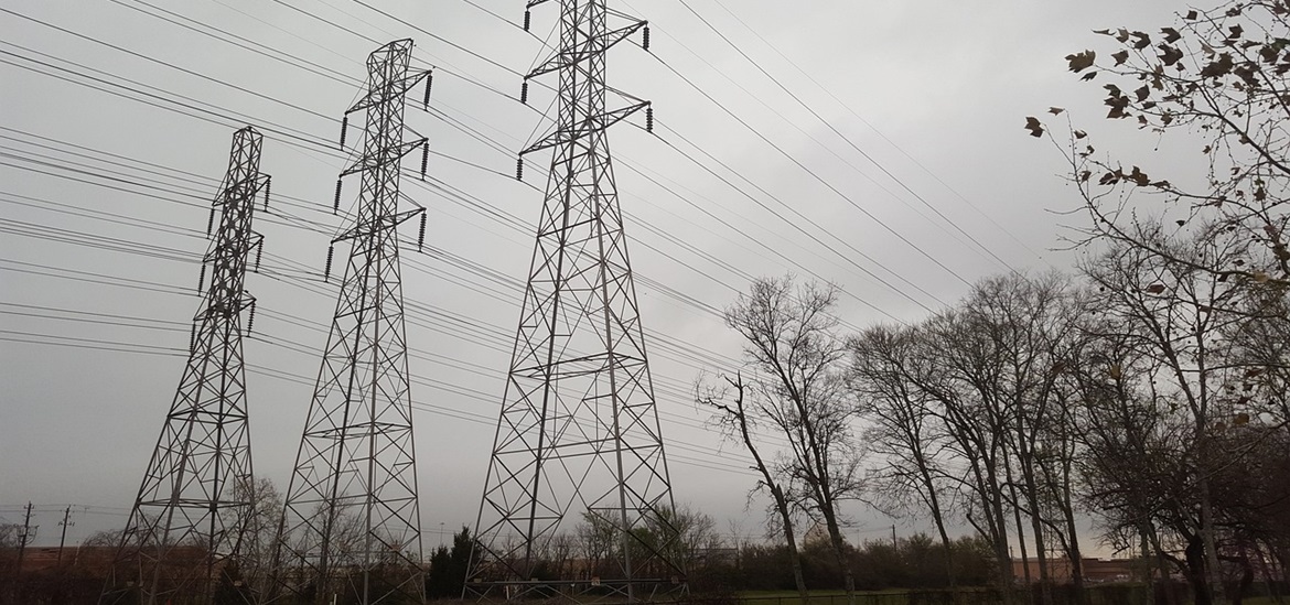 3 Power towers connected with power lines in a fiels sorrounded by woods 