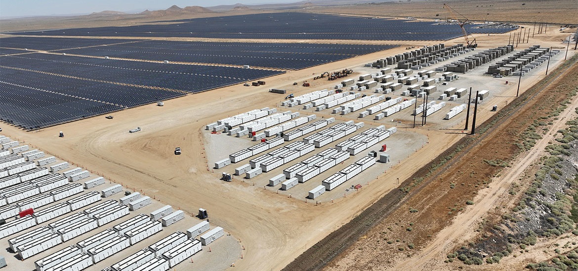 solar panels on one side and batteries on the other side of the desert- like field- bird perspective