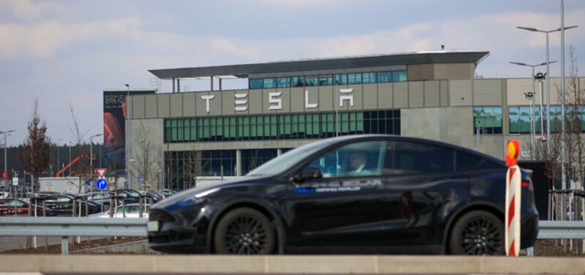 Photo of tesla factory enerance and a car driving on the road in front of it