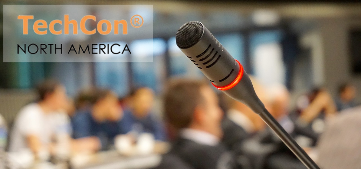 Blured image of a conference with a mic in prime focus and TechCon logo in a corner